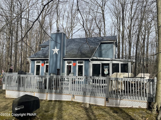 view of front of home featuring a shingled roof, a chimney, a front lawn, and a wooden deck