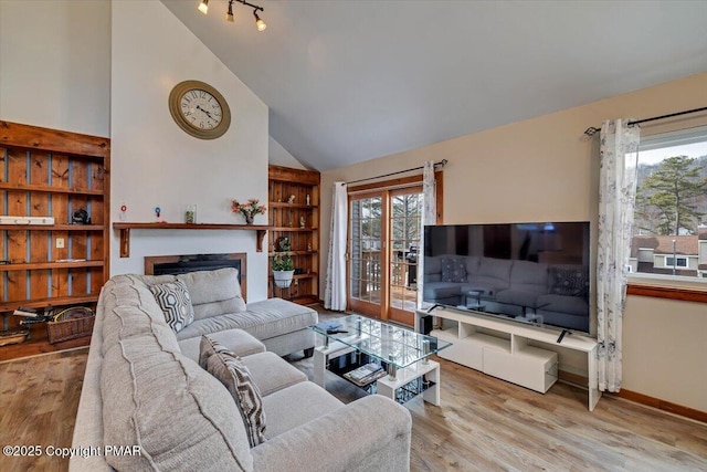 living room featuring built in shelves, a fireplace, wood finished floors, high vaulted ceiling, and baseboards