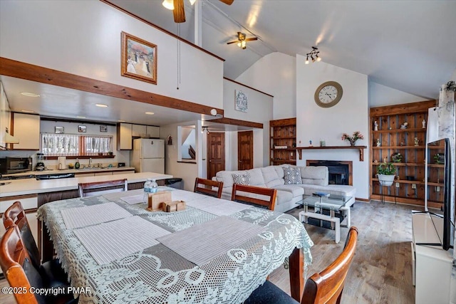 dining space featuring light wood-style floors, a fireplace, high vaulted ceiling, and ceiling fan