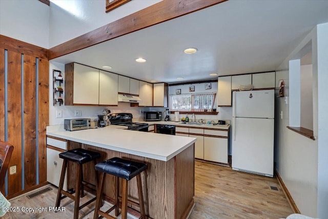 kitchen featuring light wood finished floors, visible vents, a peninsula, black appliances, and a sink