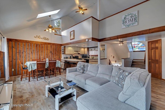 living room featuring lofted ceiling with skylight, stairway, a ceiling fan, and light wood-style floors