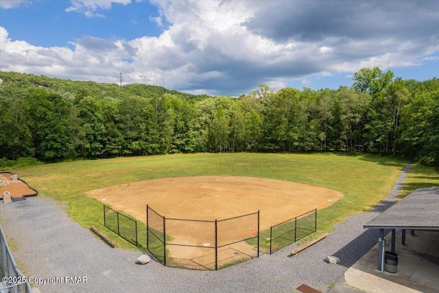 view of community with an enclosed area, a forest view, and a lawn