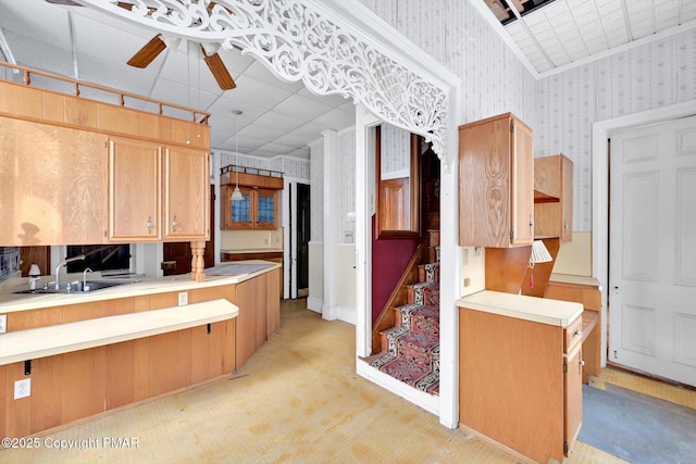 kitchen featuring light countertops, light carpet, ceiling fan, a sink, and wallpapered walls