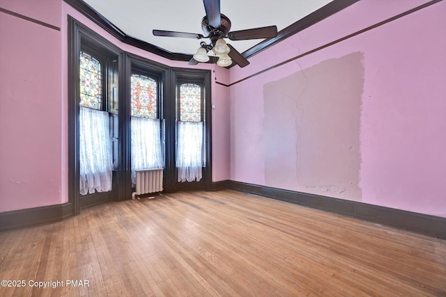 empty room featuring radiator, light wood finished floors, baseboards, and crown molding