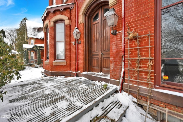 snow covered property entrance featuring brick siding