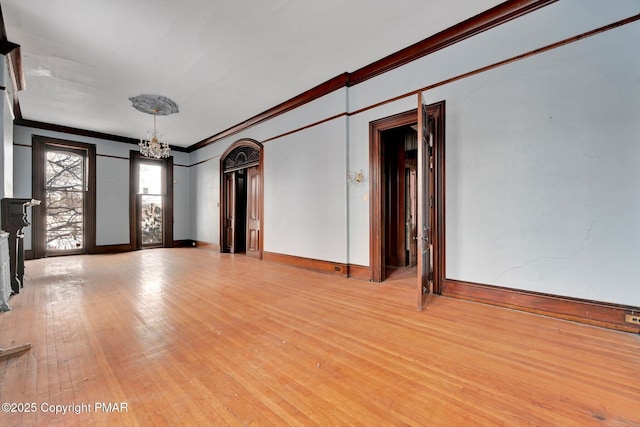 unfurnished room featuring a chandelier, baseboards, light wood-style flooring, and crown molding