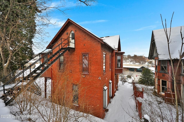 view of snowy exterior with stairs and brick siding