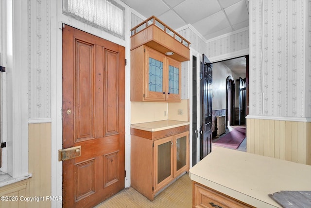 kitchen with glass insert cabinets, light countertops, crown molding, and wallpapered walls