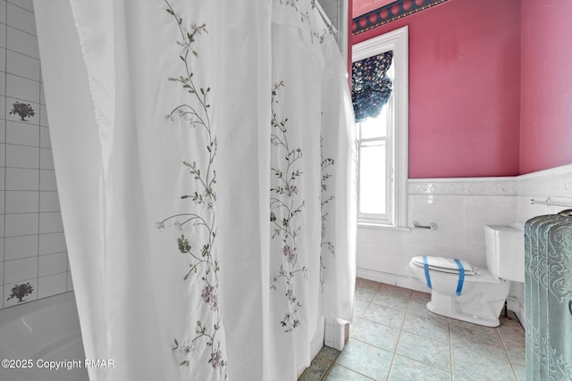 bathroom with toilet, a wainscoted wall, tile walls, tile patterned floors, and shower / bathtub combination with curtain