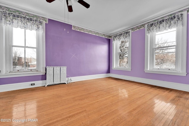 unfurnished room featuring radiator, light wood finished floors, plenty of natural light, and baseboards