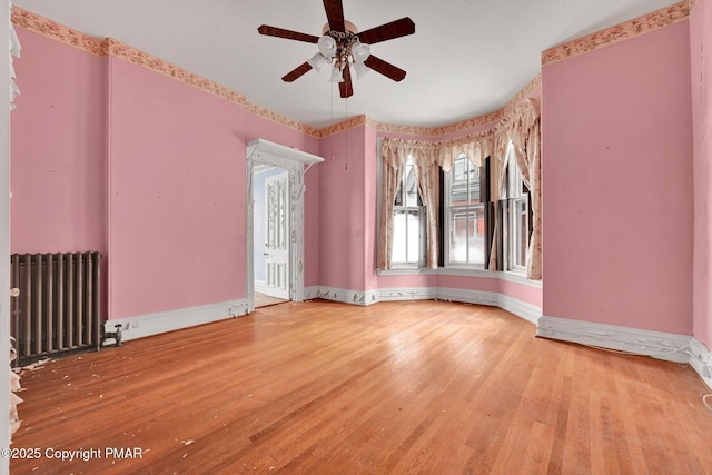 empty room with baseboards, ceiling fan, wood finished floors, and radiator