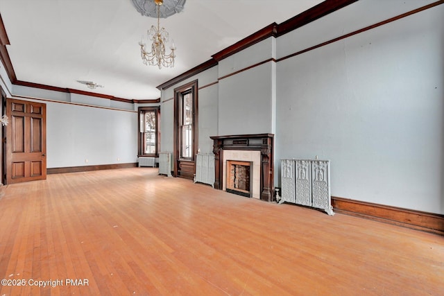 unfurnished living room featuring baseboards, hardwood / wood-style flooring, an inviting chandelier, crown molding, and a fireplace