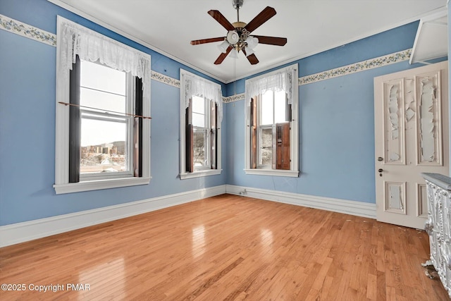 unfurnished room with a ceiling fan, wood finished floors, a wealth of natural light, and baseboards