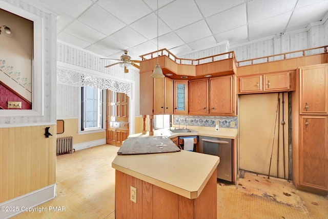 kitchen with a paneled ceiling, a wainscoted wall, light countertops, stainless steel dishwasher, and radiator heating unit