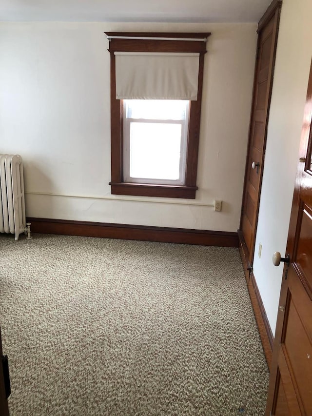 carpeted empty room with radiator heating unit and baseboards