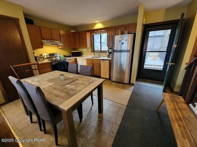 kitchen featuring a sink, under cabinet range hood, appliances with stainless steel finishes, brown cabinetry, and light countertops