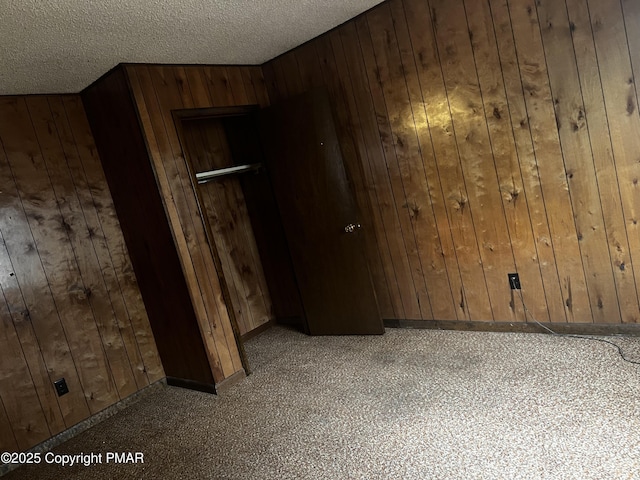 unfurnished room featuring a textured ceiling, baseboards, and wooden walls