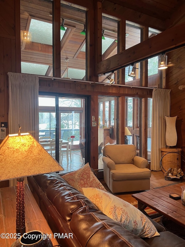 living room with beam ceiling, high vaulted ceiling, wood walls, and a skylight