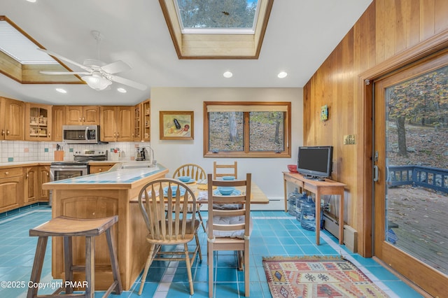 kitchen featuring kitchen peninsula, a skylight, tasteful backsplash, appliances with stainless steel finishes, and a kitchen breakfast bar