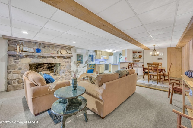 living room featuring a drop ceiling, a stone fireplace, and light colored carpet