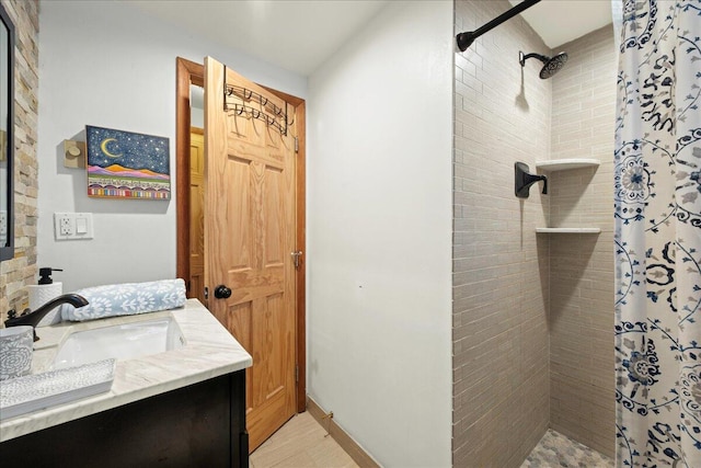 full bathroom featuring baseboards, tiled shower, and vanity