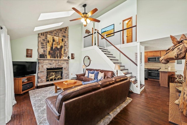 living area with dark wood-style floors, high vaulted ceiling, ceiling fan, stairs, and a stone fireplace