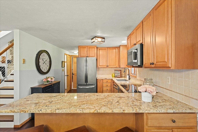 kitchen featuring a breakfast bar, a sink, tasteful backsplash, appliances with stainless steel finishes, and a peninsula