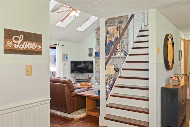 staircase with ceiling fan, vaulted ceiling with skylight, a textured ceiling, and wood finished floors