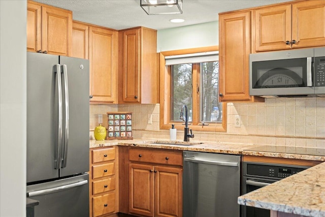 kitchen with a sink, recessed lighting, appliances with stainless steel finishes, decorative backsplash, and light stone countertops