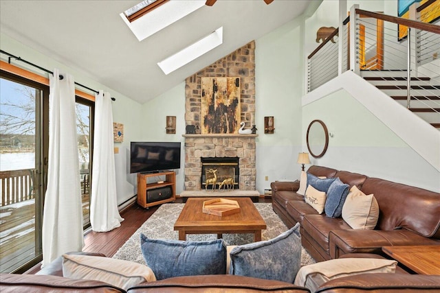 living room featuring high vaulted ceiling, wood finished floors, stairway, a stone fireplace, and a skylight