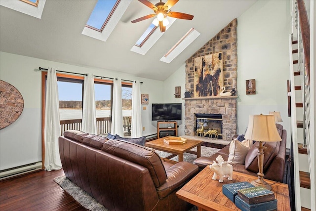 living area with ceiling fan, a stone fireplace, baseboard heating, wood finished floors, and high vaulted ceiling