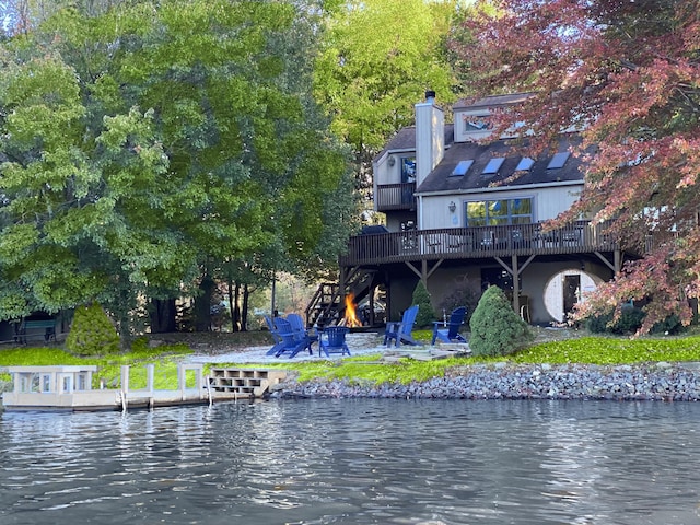 rear view of house with a chimney, a patio area, a fire pit, and a deck with water view