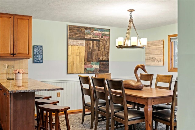 dining room featuring a chandelier, wainscoting, and a textured ceiling