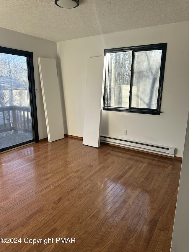 unfurnished room featuring a baseboard heating unit, wood-type flooring, and a textured ceiling