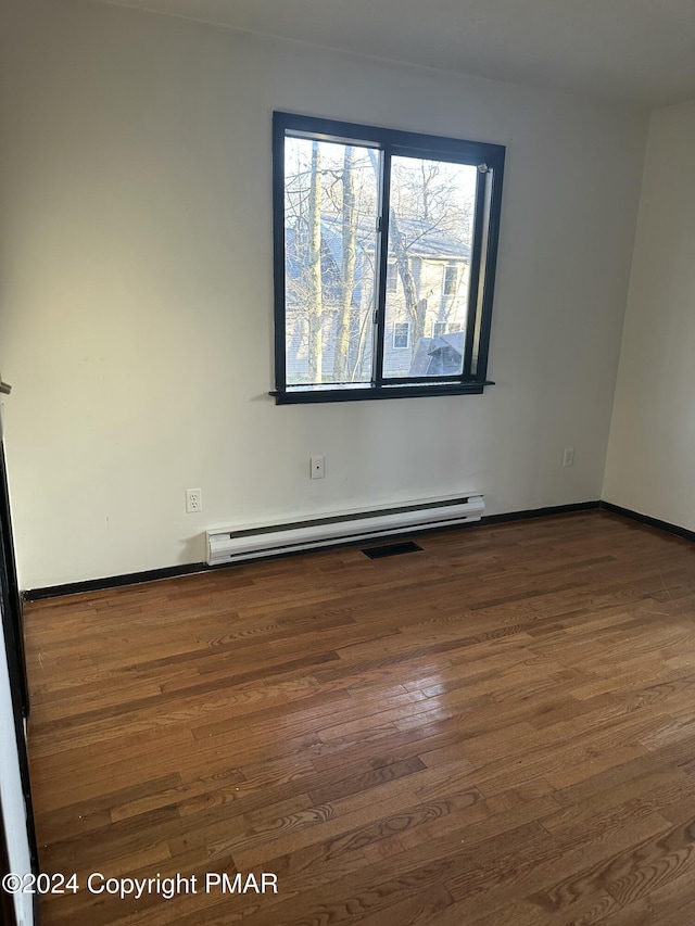 spare room with a baseboard heating unit, baseboards, and wood finished floors