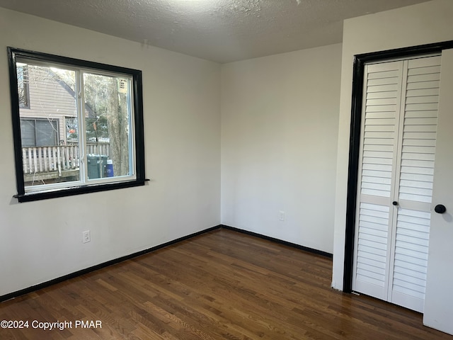 spare room featuring a textured ceiling, dark wood-type flooring, and baseboards