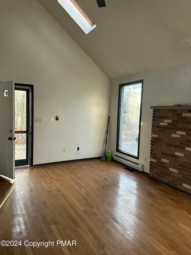 interior space featuring high vaulted ceiling, a skylight, a baseboard heating unit, and wood finished floors