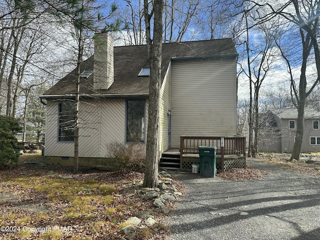 view of front facade featuring crawl space, aphalt driveway, a chimney, and a wooden deck