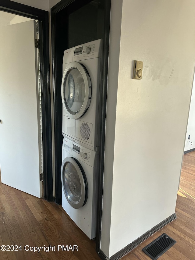 laundry area with laundry area, stacked washing maching and dryer, wood finished floors, and visible vents