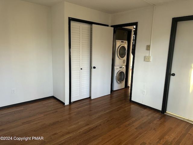 unfurnished bedroom featuring stacked washer / dryer, a closet, dark wood finished floors, and baseboards