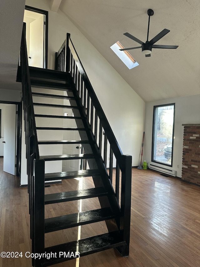 stairway featuring high vaulted ceiling, a skylight, ceiling fan, and wood finished floors