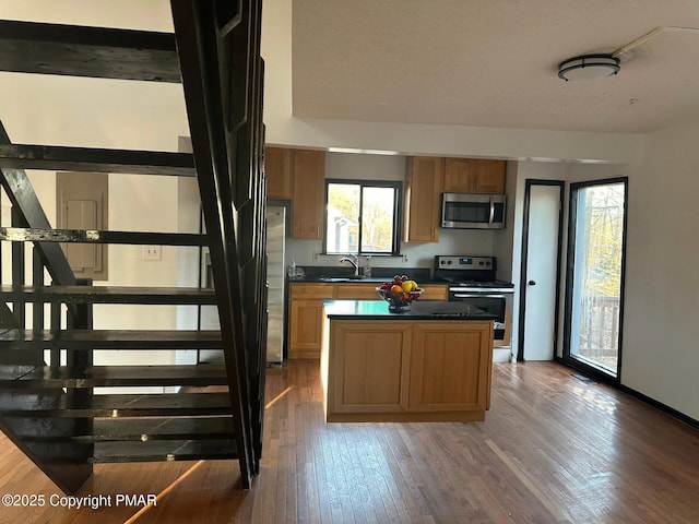 kitchen with hardwood / wood-style floors, a sink, stainless steel appliances, dark countertops, and a center island