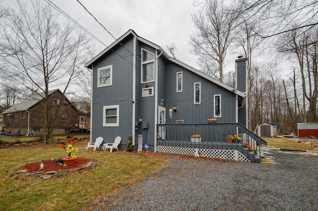 exterior space featuring a deck, an outbuilding, gravel driveway, and a chimney