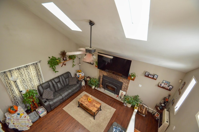 living room with vaulted ceiling with skylight, a brick fireplace, ceiling fan, and wood finished floors