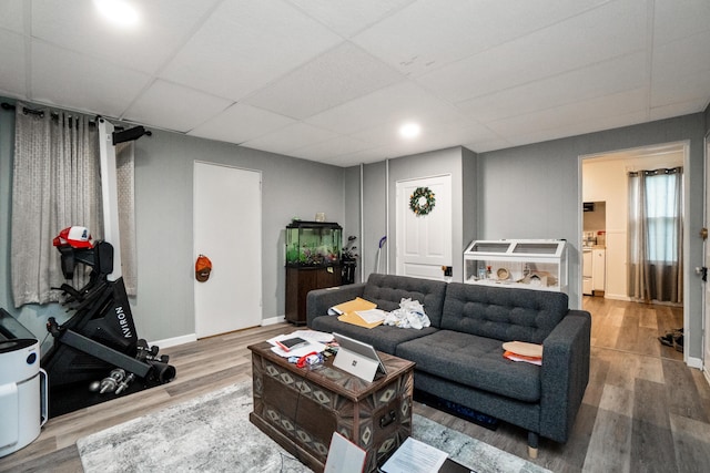 living room with wood finished floors, a drop ceiling, and baseboards