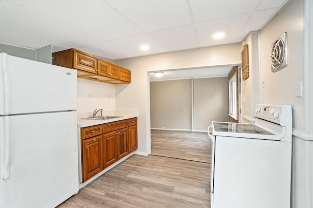 kitchen with white appliances, a sink, brown cabinetry, light wood-type flooring, and light countertops