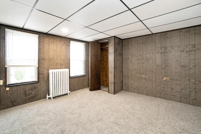 empty room featuring radiator heating unit, carpet flooring, wooden walls, and a paneled ceiling