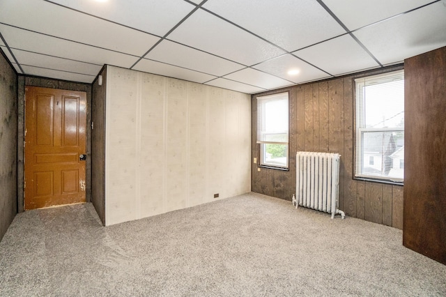 spare room featuring radiator heating unit, carpet floors, a drop ceiling, and wood walls