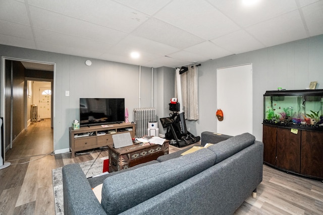 living area with radiator heating unit, wood finished floors, and a drop ceiling