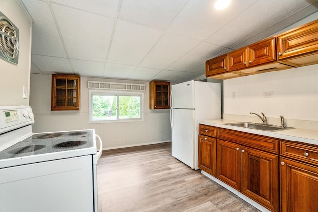 kitchen featuring white appliances, a sink, light wood-style flooring, brown cabinetry, and a drop ceiling